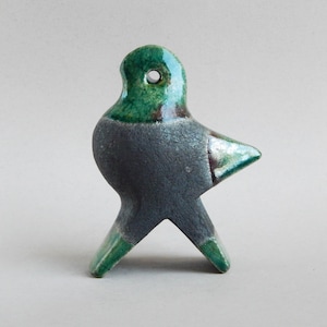 Può includere: Una statuetta di uccello in ceramica con una glassa verde e nera. L'uccello ha un becco lungo e appuntito e un piccolo foro nella testa.