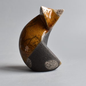 May include: A ceramic sculpture of an abstract form with a brown and black glaze. The sculpture has a rounded shape with a pointed top and a flat base.