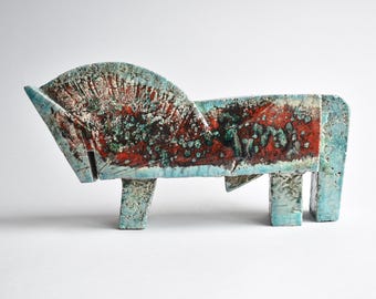 Op de afbeelding: Een keramische sculptuur van een gestileerd paard. Het paard is voornamelijk blauw met rode en groene accenten. De sculptuur heeft een textuur en een geometrisch ontwerp, met een gebogen kop en rechthoekig lichaam en poten.