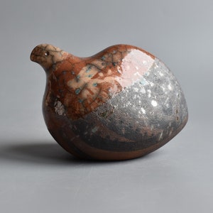 以下が含まれることがあります： 茶色、黒、白の釉薬をかけた陶器の鳥の彫刻。鳥は丸い体と小さなくちばしをしています。