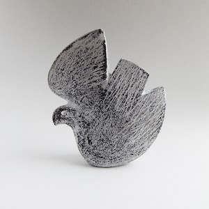 以下が含まれることがあります： 羽を広げたスタイリッシュな鳥の白黒のセラミック彫刻。彫刻はテクスチャのある表面とわずかに抽象的なデザインをしています。
