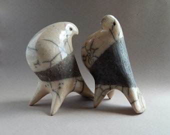 May include: Two ceramic bird sculptures with a crackled glaze finish. One bird is white with black accents, and the other is black with white accents.