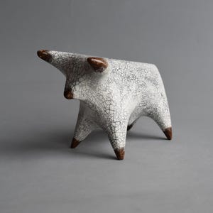 May include: A ceramic bull figurine featuring a white glaze with a prominent black crackle pattern. The bull has four legs, two horns, and a snout, all accented with a solid brown finish at the tips, creating a distinct contrast against the body.