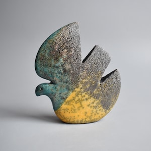 May include: A ceramic sculpture of a stylized bird with a yellow, blue, and black glaze. The bird is in a flying pose with its wings spread.