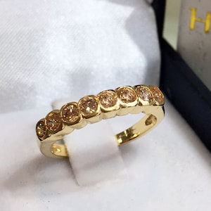 May include: A gold band ring with a row of small, round, light brown gemstones.