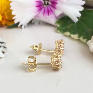Puede incluir: Un par de pendientes de oro con piedras rosas engastadas en un dise&ntilde;o de corona.