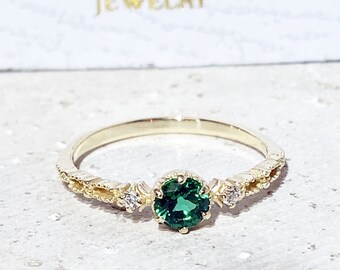 Puede incluir: Un delicado anillo de oro con una piedra preciosa verde y pequeñas piedras blancas en la banda. El anillo tiene un diseño de inspiración vintage.