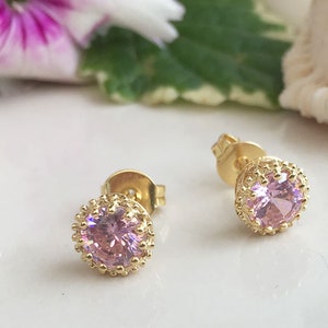 Puede incluir: Un par de pendientes de bot&oacute;n de oro con piedras redondas rosas engastadas en un marco decorativo de oro.