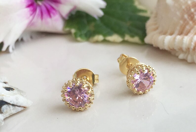 Puede incluir: Un par de pendientes de bot&oacute;n de oro con piedras redondas rosas engastadas en un marco decorativo de oro.