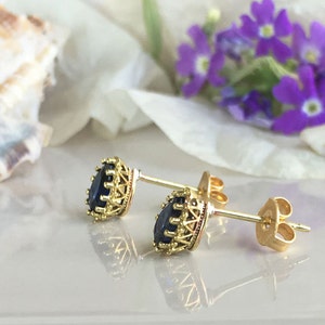 Puede incluir: Un par de pendientes de bot&oacute;n de oro con una piedra preciosa azul oscuro engastada en un marco de oro decorativo.