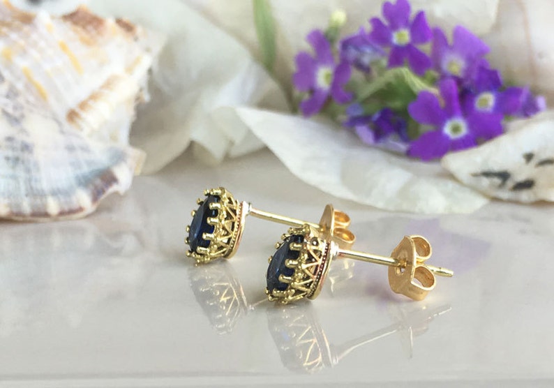 Puede incluir: Un par de pendientes de bot&oacute;n de oro con una piedra preciosa azul oscuro engastada en un marco de oro decorativo.