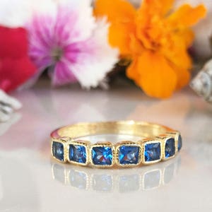 Könnte beinhalten: Ein Goldring mit sieben quadratischen blauen Edelsteinen.