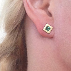 May include: A pair of gold square earrings with a small green gemstone in the center.
