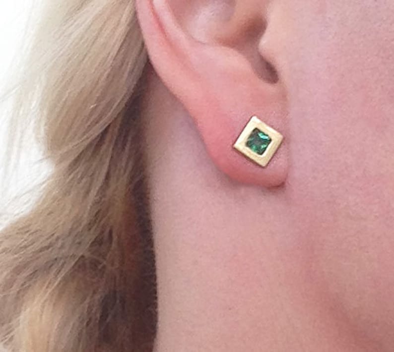 May include: A pair of gold square earrings with a small green gemstone in the center.