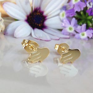 May include: A pair of gold-toned stud earrings shaped like hands. The earrings are small and delicate, and they would make a great gift for someone special.
