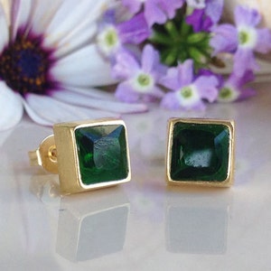May include: A pair of gold square earrings with green gemstone accents.