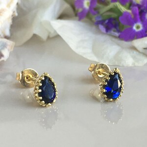 Puede incluir: Un par de pendientes de bot&oacute;n de oro con una piedra preciosa azul en forma de l&aacute;grima engastada en un engaste de oro.