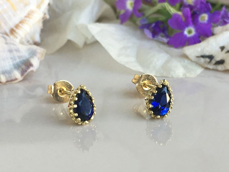 Puede incluir: Un par de pendientes de bot&oacute;n de oro con una piedra preciosa azul en forma de l&aacute;grima engastada en un engaste de oro.