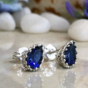 Puede incluir: Un par de pendientes de plata con una piedra preciosa azul en forma de l&aacute;grima engastada en un dise&ntilde;o de corona.