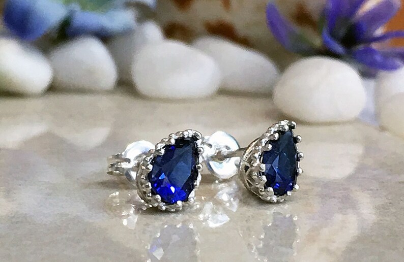 Puede incluir: Un par de pendientes de plata con una piedra preciosa azul en forma de l&aacute;grima engastada en un dise&ntilde;o de corona.