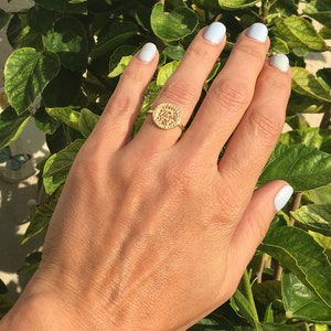 May include: A gold ring with a circular design featuring intricate cutouts. The ring is worn on the middle finger of a hand with light blue nail polish.