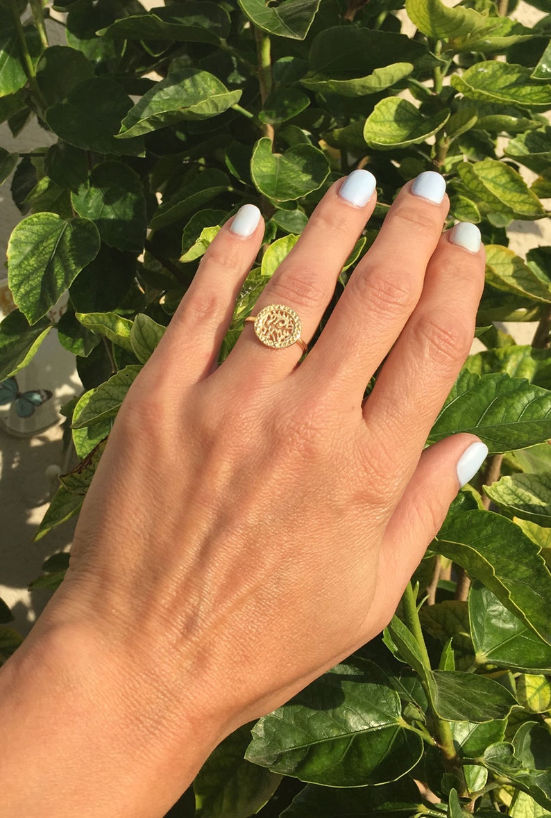 May include: A gold ring with a circular design featuring intricate cutouts. The ring is worn on the middle finger of a hand with light blue nail polish.