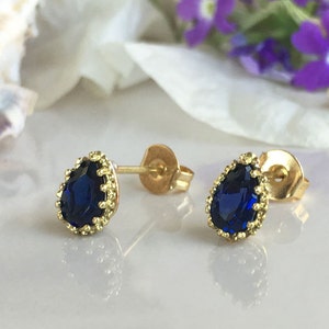 Puede incluir: Un par de pendientes de bot&oacute;n de oro con una piedra preciosa azul en forma de l&aacute;grima engastada en un dise&ntilde;o de filigrana de oro.