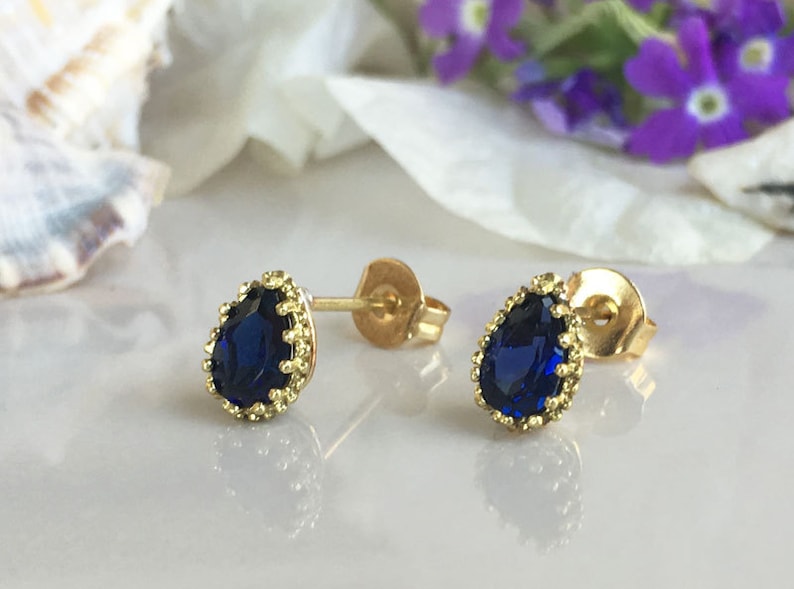Puede incluir: Un par de pendientes de bot&oacute;n de oro con una piedra preciosa azul en forma de l&aacute;grima engastada en un dise&ntilde;o de filigrana de oro.