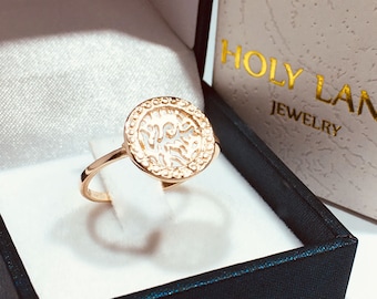 Könnte beinhalten: Ein goldener Ring mit einem runden, durchbrochenen Design mit filigranen Details. Der Ring wird in einer schwarz-weißen Schachtel mit der Aufschrift "HOLY LAND JEWELRY" auf dem Deckel präsentiert.