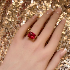 Puede incluir: Un anillo de oro con una piedra rectangular roja grande.