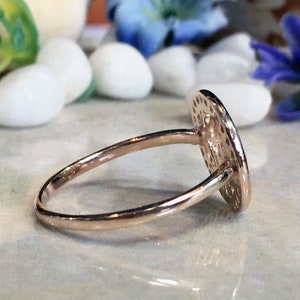 May include: A gold ring with a round, textured, hammered design. The ring is on a white surface.