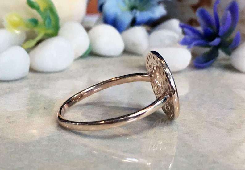 May include: A gold ring with a round, textured, hammered design. The ring is on a white surface.