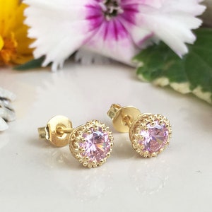 Puede incluir: Un par de pendientes de oro con una piedra preciosa rosa en el centro de cada pendiente. Los pendientes tienen un dise&ntilde;o delicado y ornamentado alrededor de la piedra preciosa.