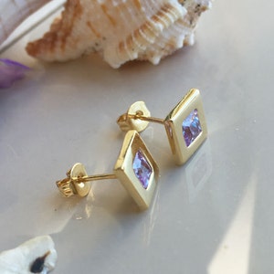May include: A pair of gold square stud earrings with small purple cubic zirconia stones.