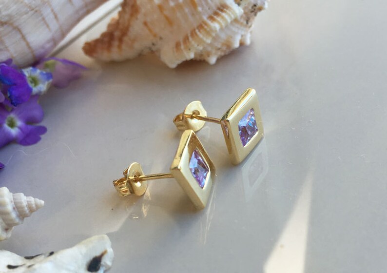 May include: A pair of gold square stud earrings with small purple cubic zirconia stones.