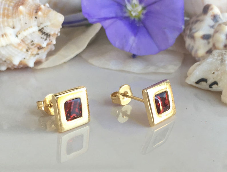 May include: A pair of gold square stud earrings with red gemstone accents.
