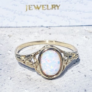 May include: A gold ring featuring an oval opal gemstone set in a delicate filigree design. The ring is displayed against a white background.