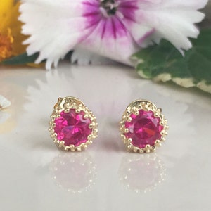 May include: A pair of gold earrings with pink round gemstones set in a gold filigree design.