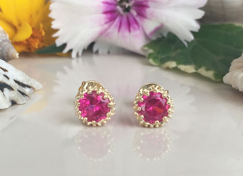 May include: A pair of gold earrings with pink round gemstones set in a gold filigree design.