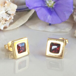 May include: A pair of gold square stud earrings with red gemstone accents.