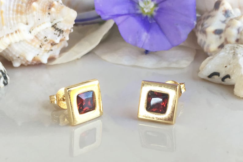 May include: A pair of gold square stud earrings with red gemstone accents.