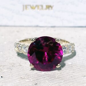 May include: A gold ring with a large, round, deep red gemstone surrounded by smaller, clear gemstones.