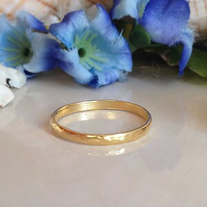 May include: A simple gold band ring with a hammered texture. The ring is on a white surface.