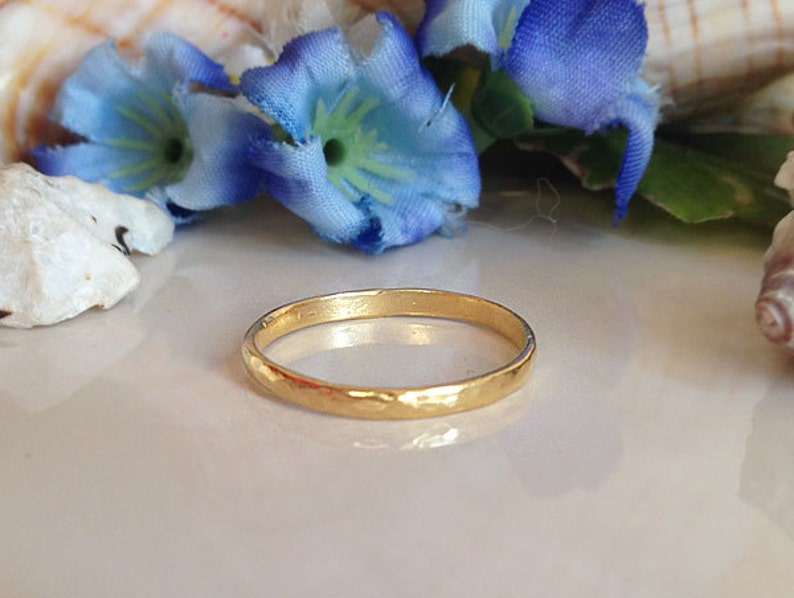 May include: A simple gold band ring with a hammered texture. The ring is on a white surface.