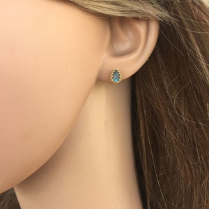 May include: A pair of gold stud earrings with a teardrop-shaped blue gemstone set in a gold bezel.