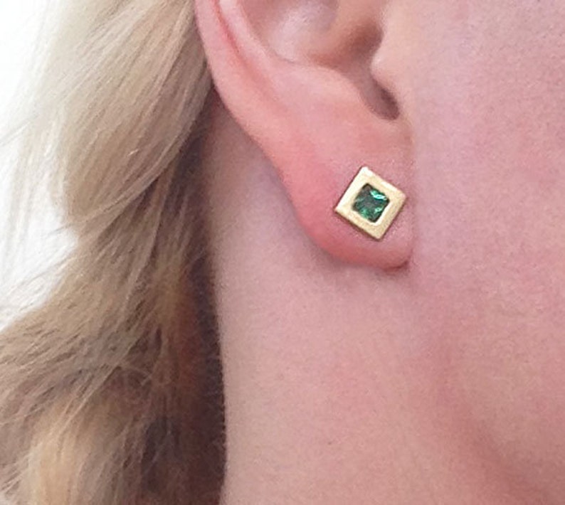 May include: A pair of gold square earrings with a small green gemstone in the center.