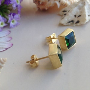 May include: A pair of gold earrings with square green gemstones. The earrings have a simple design and are perfect for everyday wear.