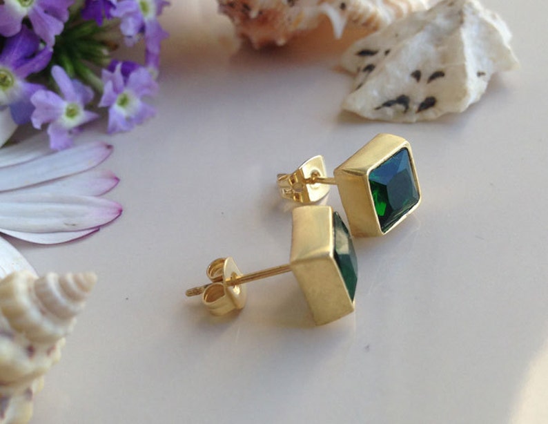 May include: A pair of gold earrings with square green gemstones. The earrings have a simple design and are perfect for everyday wear.