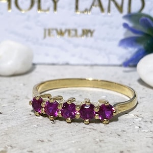 May include: A gold band ring with five pink gemstones set in a curved row.
