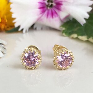 Puede incluir: Un par de pendientes de bot&oacute;n de oro con un centro de piedra preciosa rosa y un halo de cuentas.